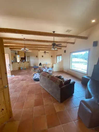 Spacious living area with terracotta floors, exposed wooden beams, and a brown sofa.