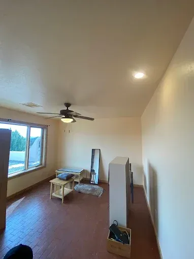 Room with red floor, tan walls, window, ceiling fan, small table, mirror.