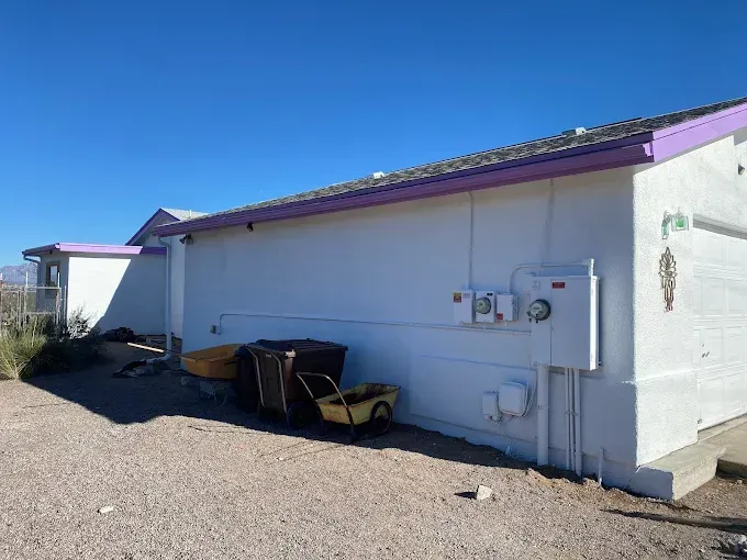 White building with purple trim, electrical boxes, and a yellow toy wagon on gravel.