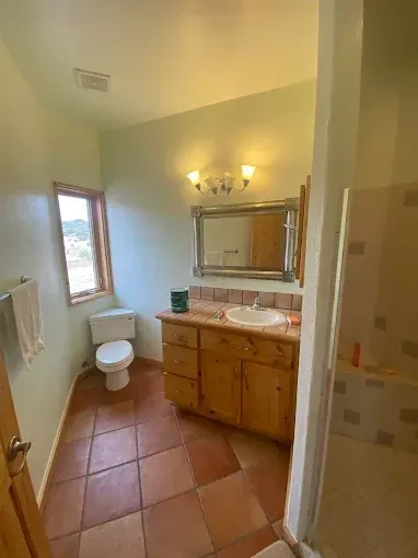 Bathroom with light green walls, wooden vanity, terracotta floor, and a window.