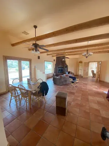Spacious room with dining table, fireplace, and exposed ceiling beams. Brown tile floor and tan walls.