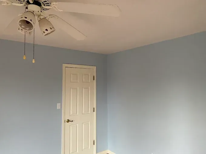 Blue-painted bedroom with white door, ceiling, and ceiling fan.