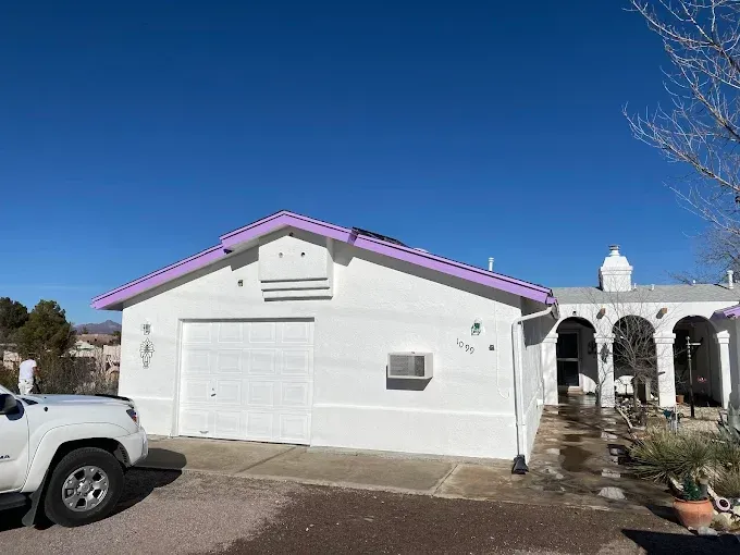 White house with purple trim, garage door, AC unit, and a vehicle on a sunny day.