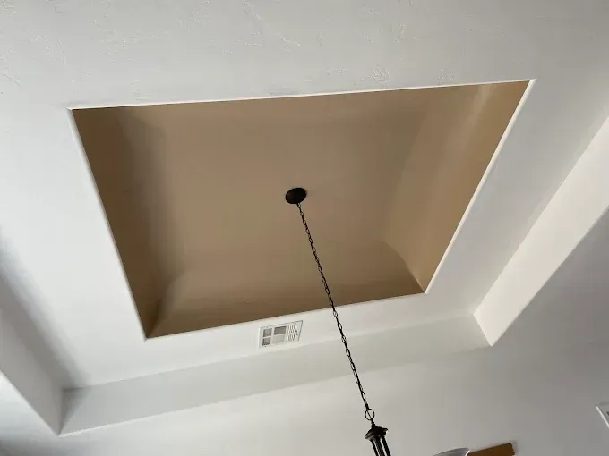 Beige recessed ceiling with a light fixture hanging down. White surrounding ceiling.