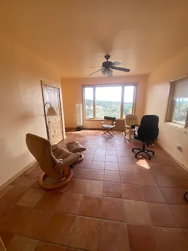 Room with orange walls, tiled floor, windows, recliner, office chair, and ceiling fan.