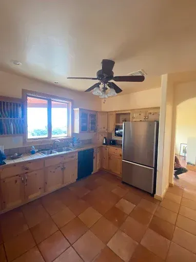Kitchen with wood cabinets, stainless steel fridge, and terracotta tile floor.