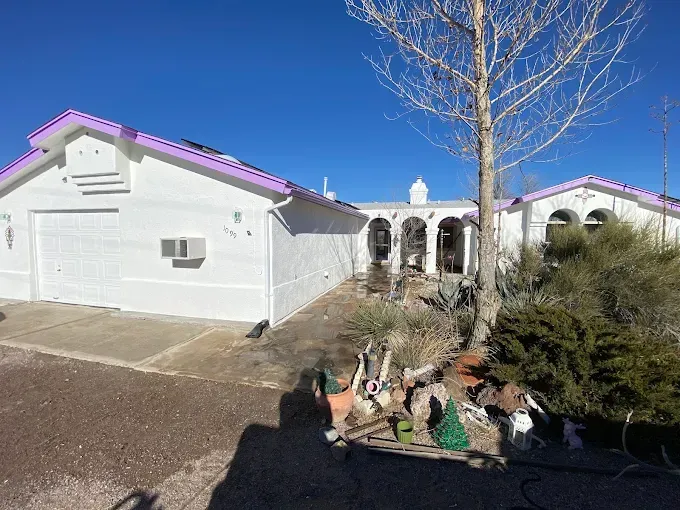 White house with purple roof trim and arched entryway; front yard with dry vegetation.