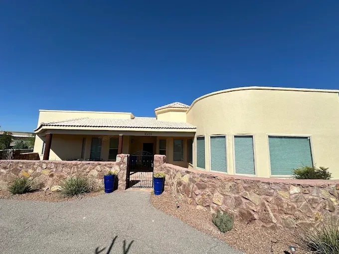 A tan stucco home with a stone wall and blue pots against a bright blue sky.
