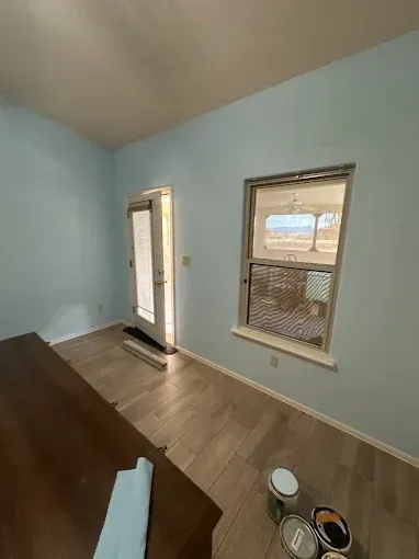 Room with blue walls, window, door, wood floor, and paint cans.