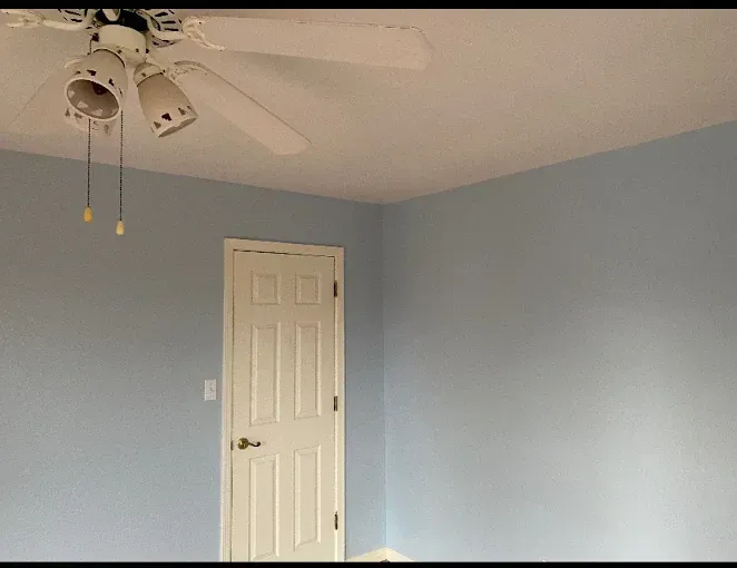 Room with light blue walls, white ceiling, door, and ceiling fan.