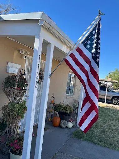 American flag hanging outside a beige house with a porch, pumpkins on display.