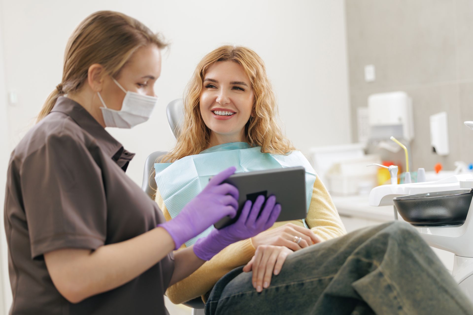 A dental professional wearing purple gloves showing a tablet to a patient seated in a dental chair.