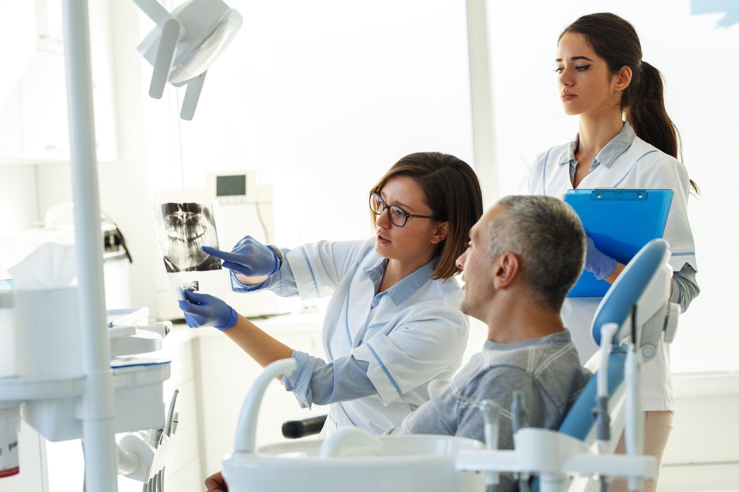 Dentist showing dental X-ray to a patient in a clinic, assistant holding a clipboard.