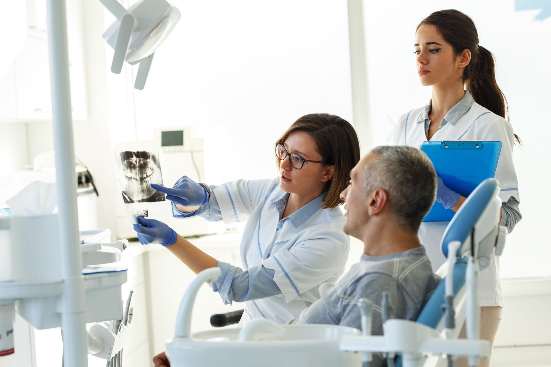 Dentist showing dental X-ray to a patient in a clinic, assistant holding a clipboard. Dentist showing dental X-ray to a patient in a clinic, assistant holding a clipboard.