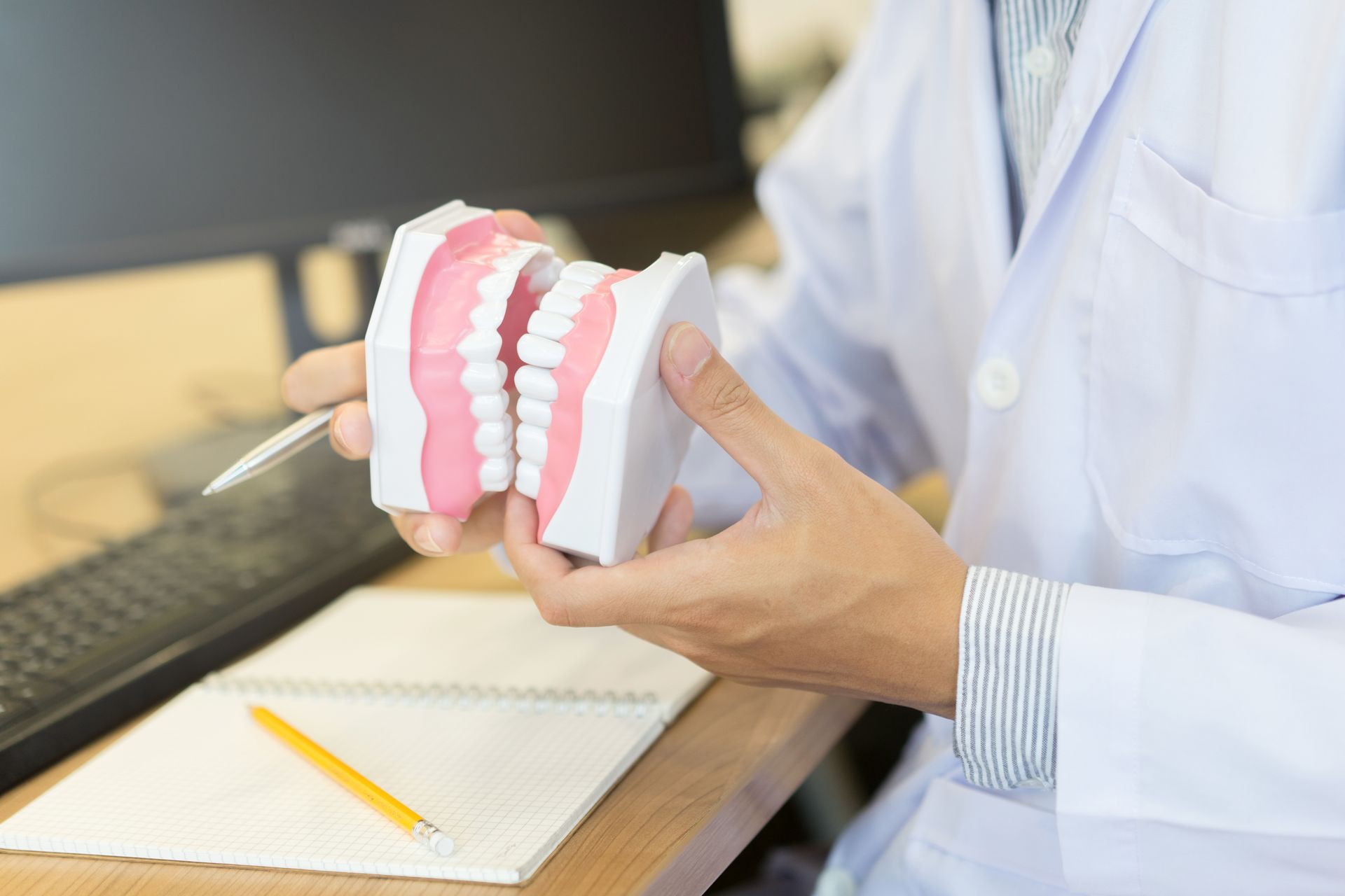 A close-up of a dentist’s hand holding model teeth in front of his computer.