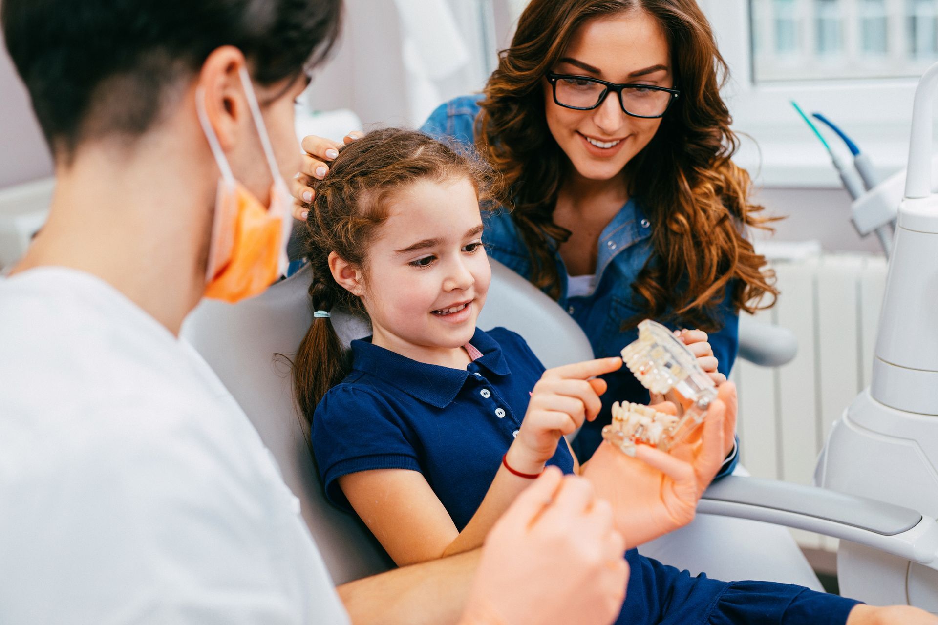 A family dentist at Osage Dental Associates in Blaine, MN, teaches a girl and her mother how to maintain healthy teeth