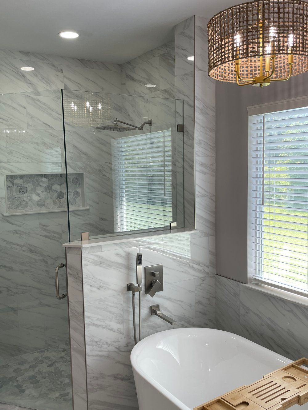 A bathroom with a tub , shower , mirror and window.