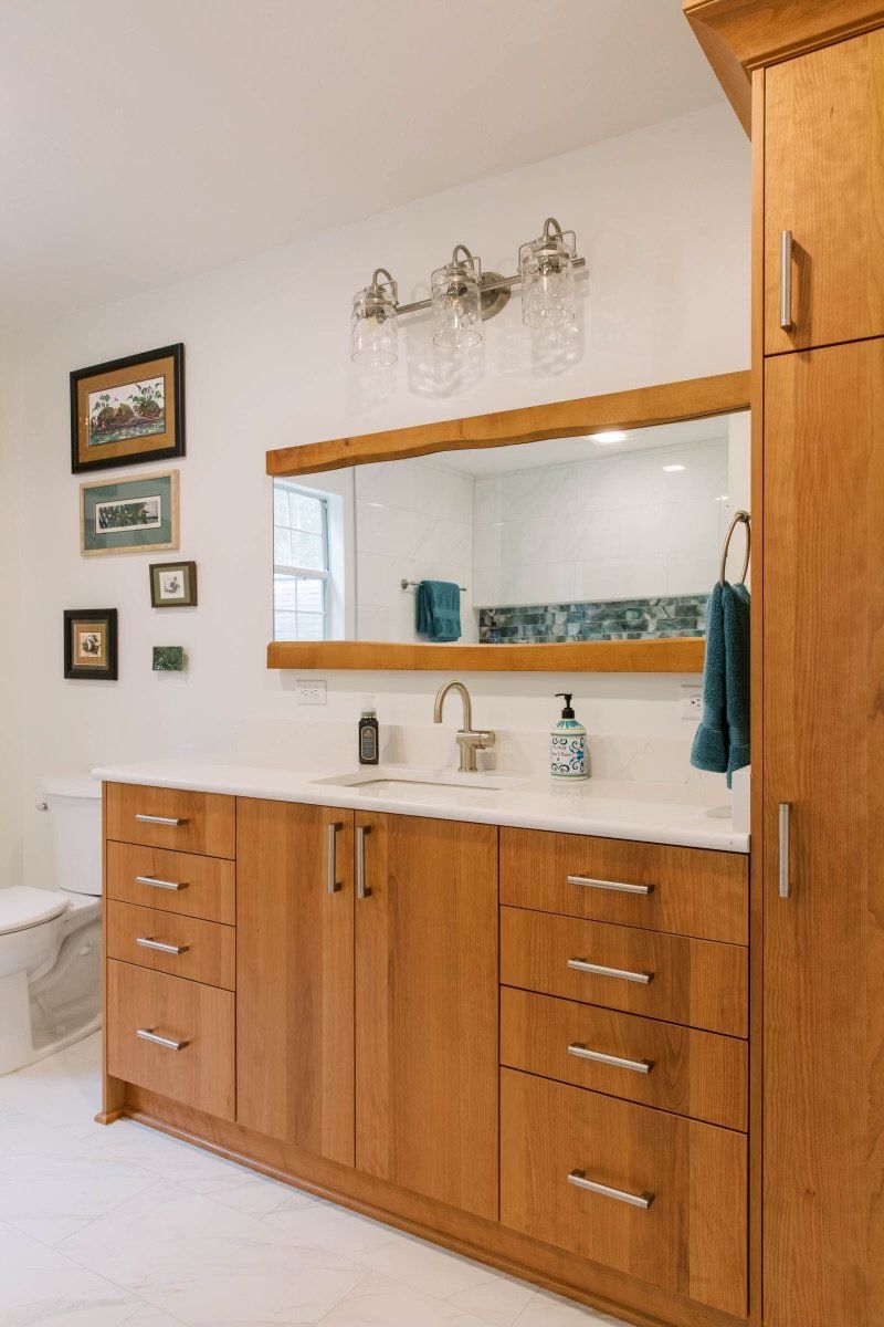 A bathroom with a sink , mirror , cabinets and drawers.