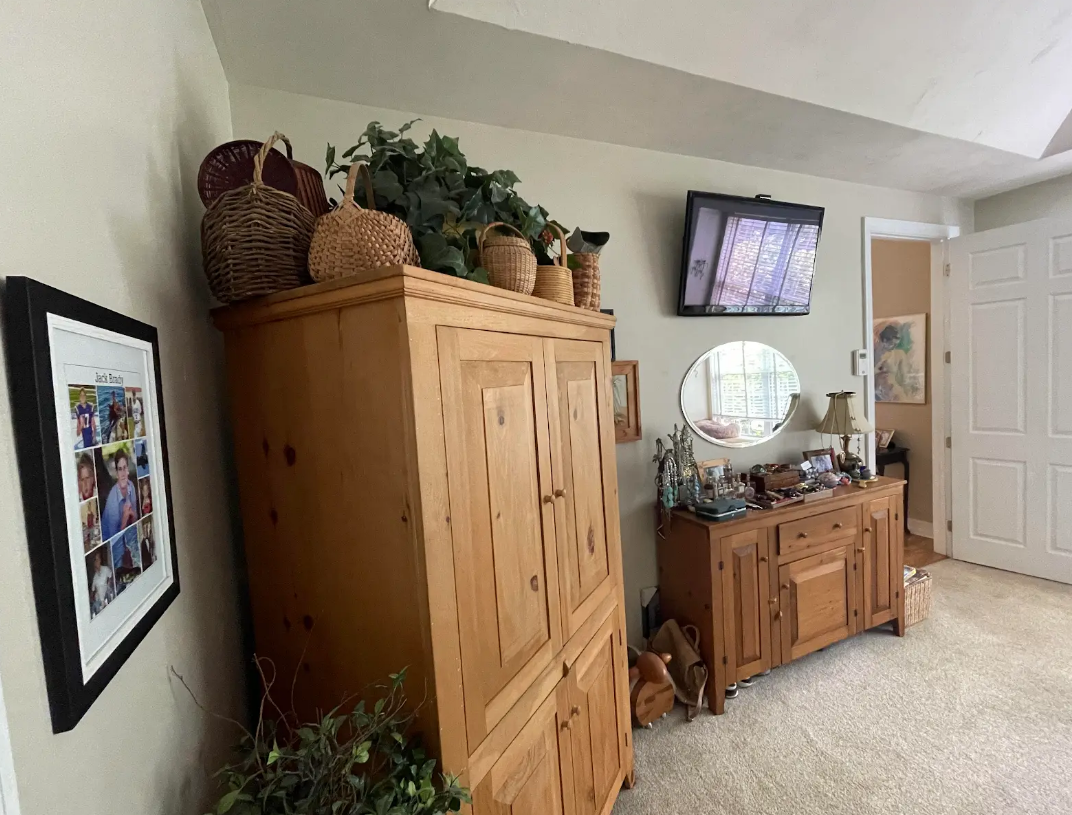 A bedroom with a wooden cabinet , dresser , mirror and television.