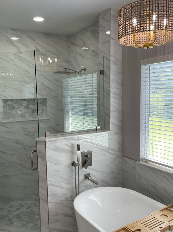 A bathroom with a tub , shower , mirror and window.
