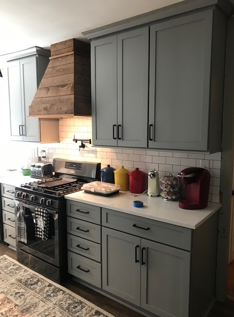 A kitchen with gray cabinets , a stove , and a hood.
