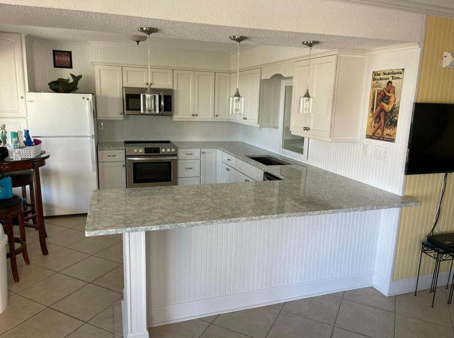 A kitchen with white cabinets , granite counter tops , stainless steel appliances and a flat screen tv.