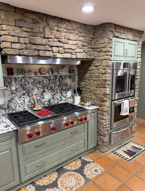 A kitchen with stainless steel appliances and a stone wall.