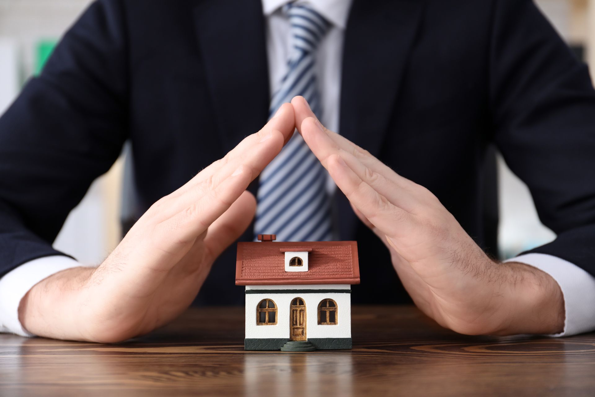 Man in office wear is protecting a house model.