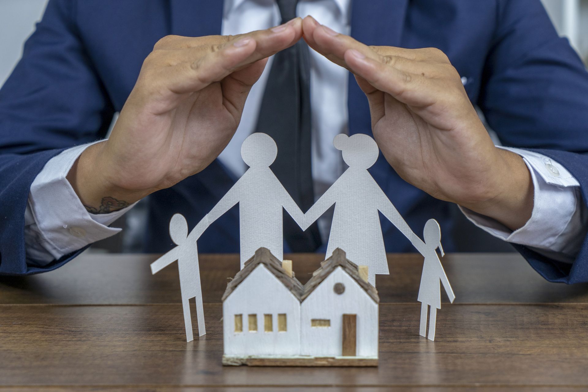 A man in a suit and tie is covering a paper cut out of a family and a house.