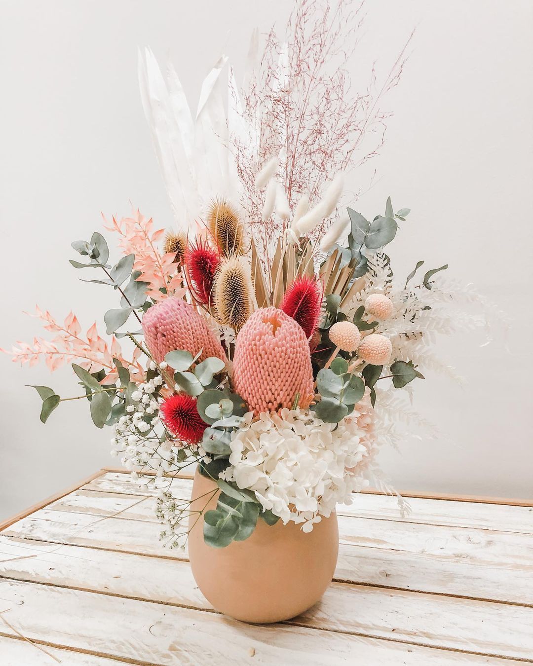 A Vase Filled With Dried Flowers is Sitting on a Wooden Table — Suncoast Flowers in Birtinya, QLD