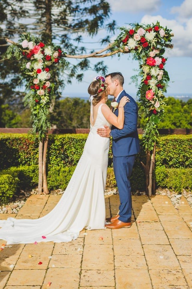 A Bride and Groom Are Kissing Under a Floral Arch at Their Wedding — Suncoast Flowers in Birtinya, QLD