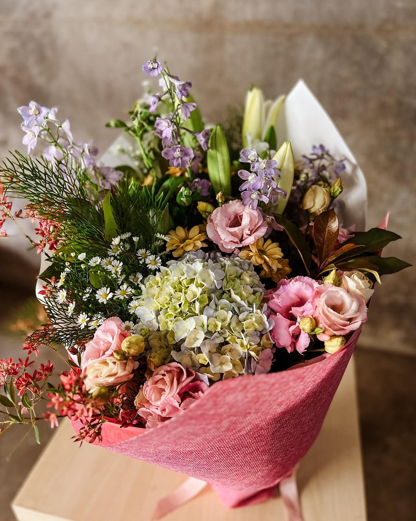 A Bouquet of Flowers Wrapped in Pink Paper is Sitting on Top of a Wooden Box