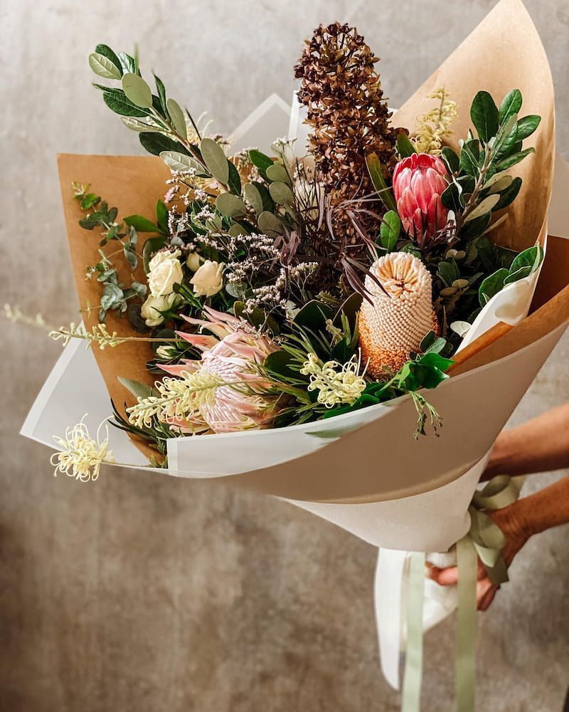 A Person is Holding a Bouquet of Flowers Wrapped in Brown Paper — Suncoast Flowers in Caloundra, QLD