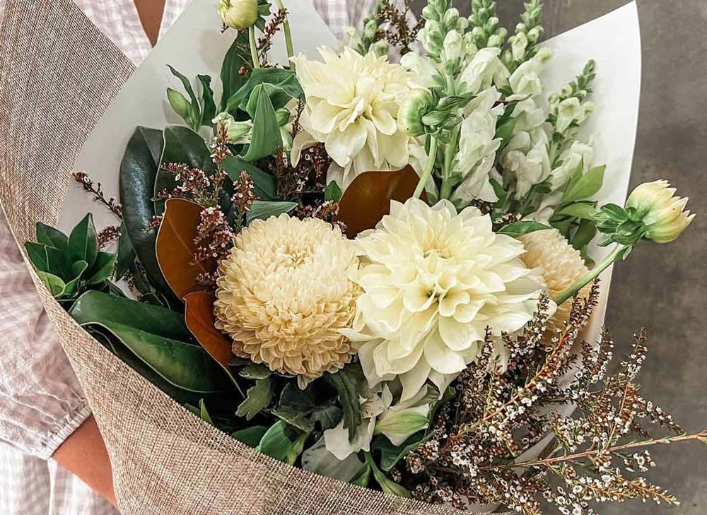 A Person is Holding a Bouquet of White Flowers Wrapped in Newspaper — Suncoast Flowers in Birtinya, QLD
