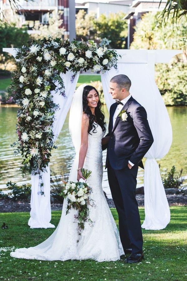 A Bride and Groom Are Posing for a Picture in Front of a Floral Arch — Suncoast Flowers in Birtinya, QLD