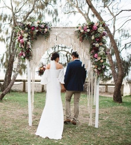 A Bride and Groom Are Standing Under a Macrame Arch Decorated With Flowers — Suncoast Flowers in Birtinya, QLD