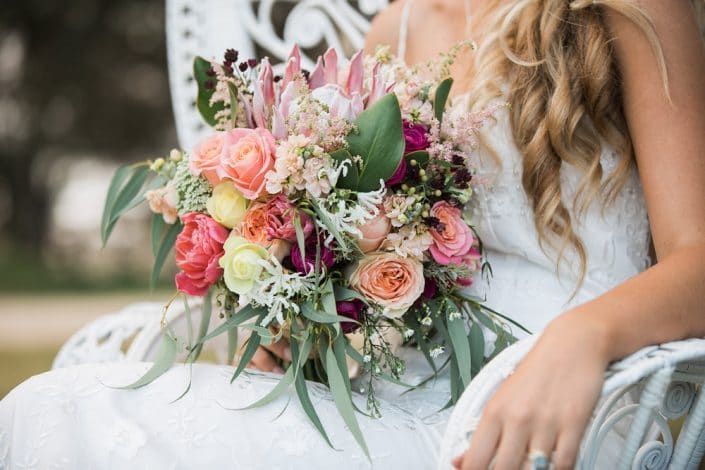 A Bride in a White Dress is Sitting on a Bench Holding a Bouquet of Flowers — Suncoast Flowers in Birtinya, QLD