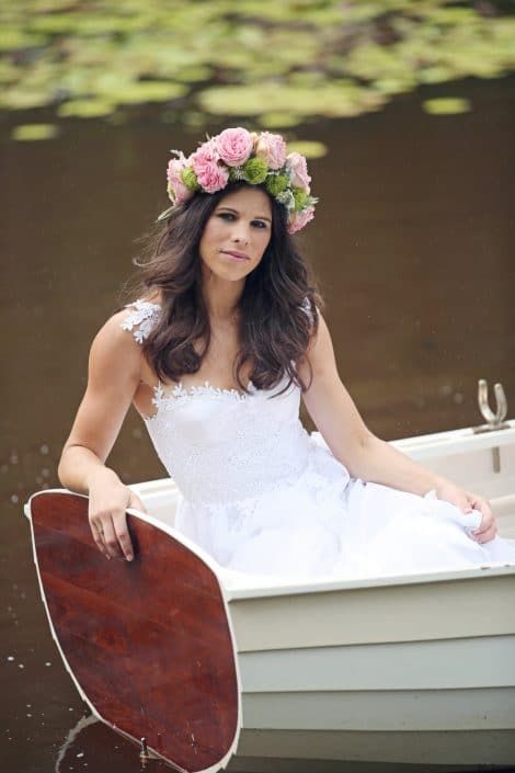 A Woman in a Wedding Dress is Sitting in a Boat With a Flower Crown on Her Head — Suncoast Flowers in Birtinya, QLD