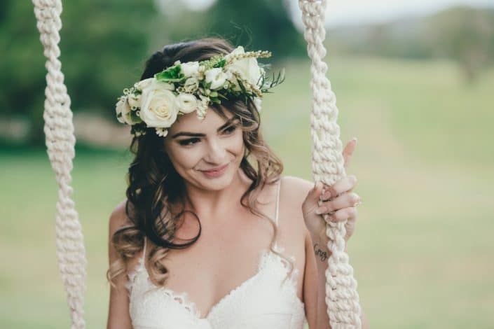 A Woman in a Wedding Dress is Sitting on a Swing With a Flower Crown on Her Head — Suncoast Flowers in Birtinya, QLD
