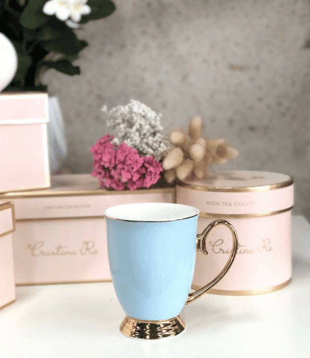 Elegant blue and gold-handled teacup displayed with pink gift boxes and flowers.