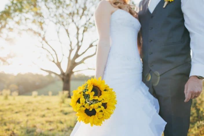 Bride and Groom Are Standing in a Field Holding Hands and the Bride is Holding a Bouquet — Suncoast Flowers in Birtinya, QLD