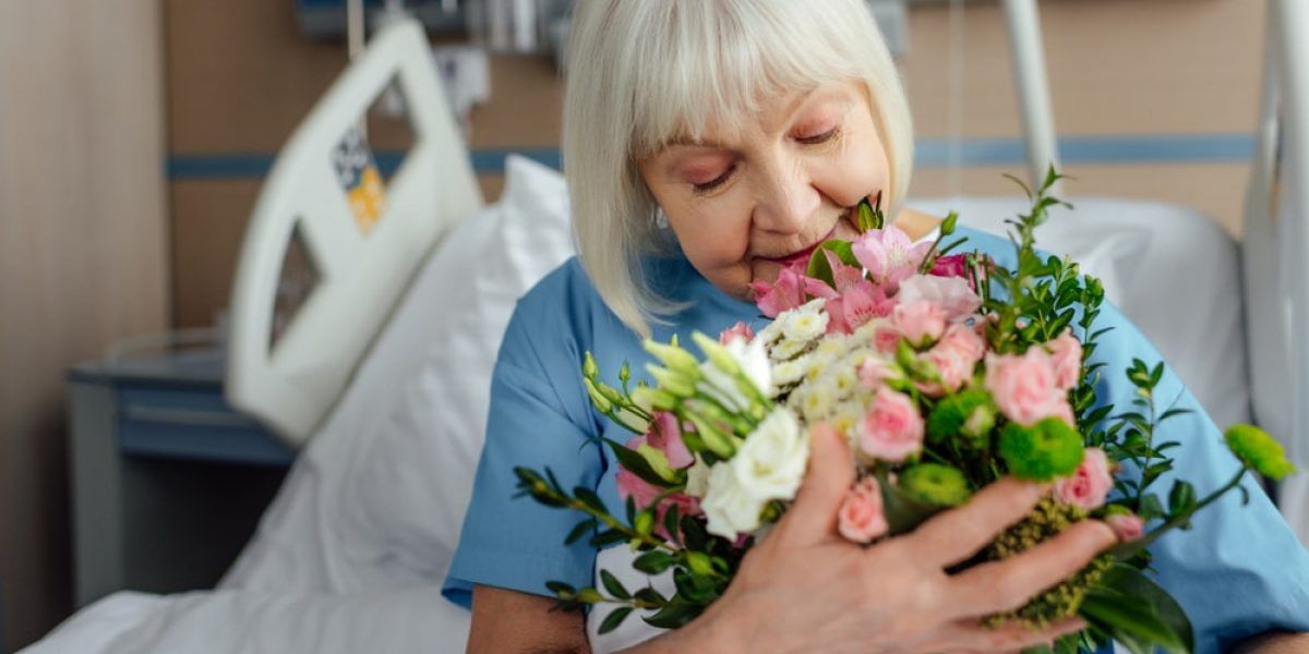 An Elderly Woman is Sitting in a Hospital Bed Holding a Bouquet of Flowers — Suncoast Flowers in Birtinya, QLD
