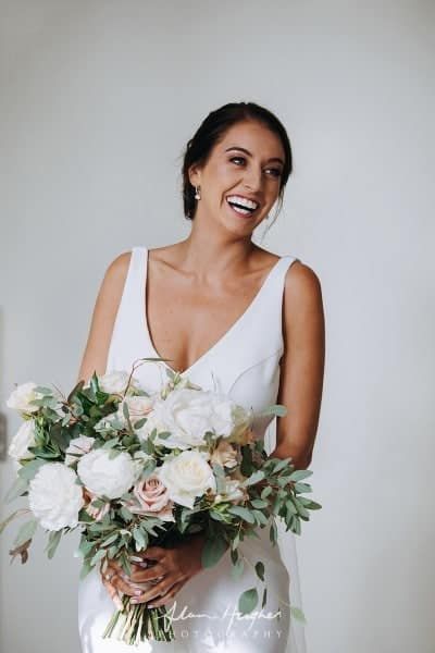 A Woman in a White Dress is Holding a Bouquet of Flowers and Smiling — Suncoast Flowers in Birtinya, QLD