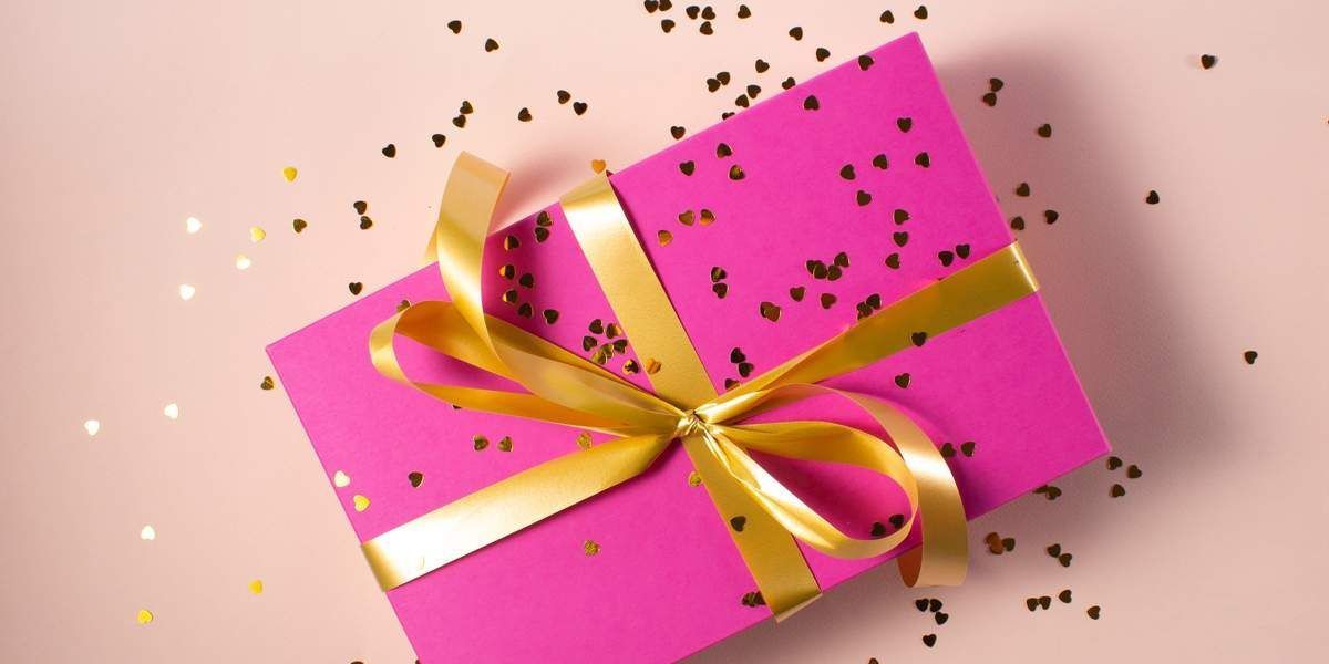 A Pink Gift Box With a Gold Ribbon and Bow on a Pink Background — Suncoast Flowers in Buderim, QLD