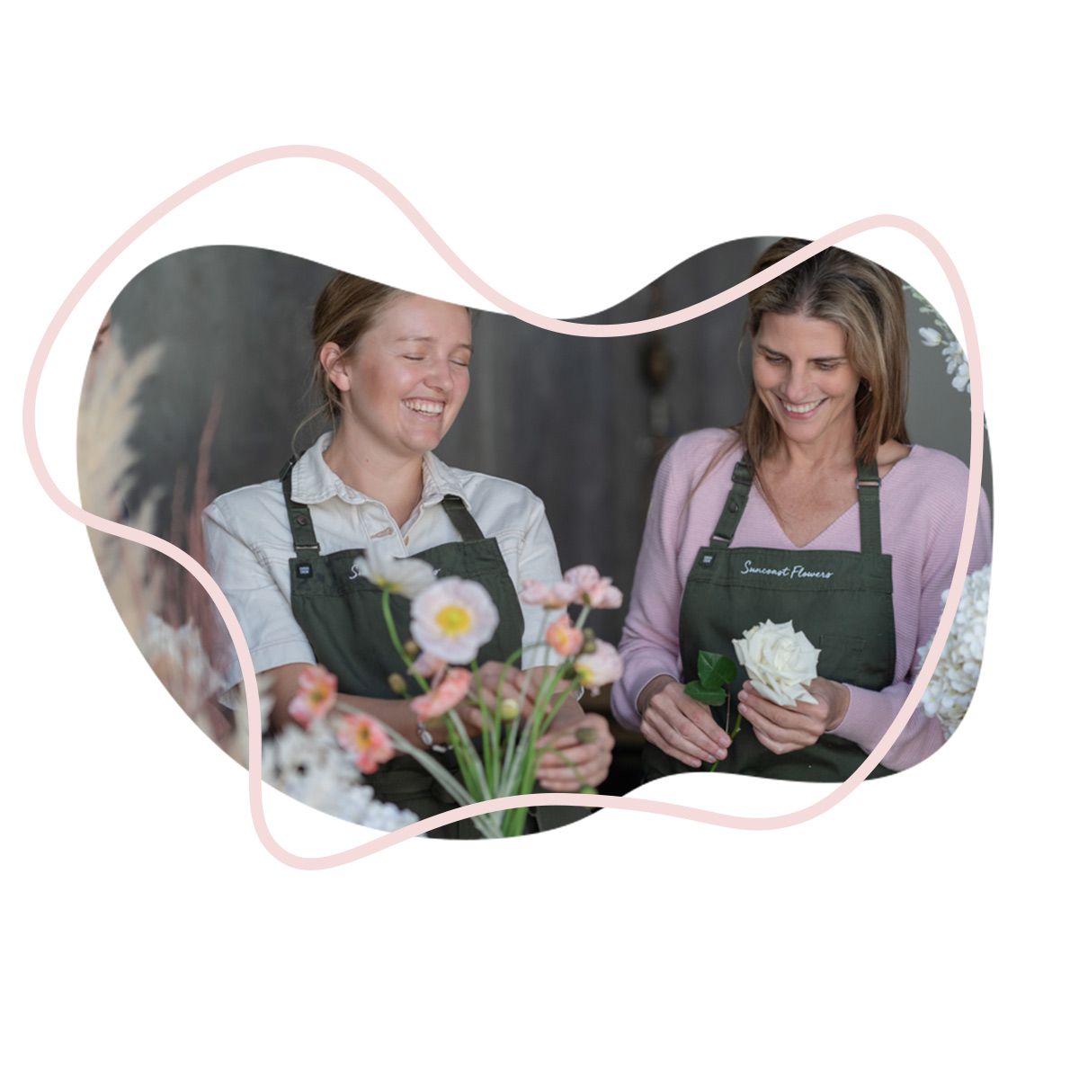 Two Women in Aprons Are Holding Flowers and Smiling — Suncoast Flowers in Birtinya, QLD