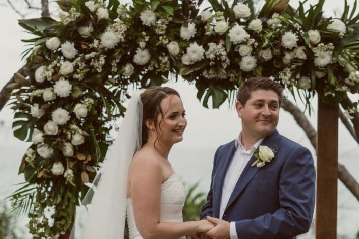 A Bride and Groom Are Holding Hands Under a Floral Arch — Suncoast Flowers in Birtinya, QLD