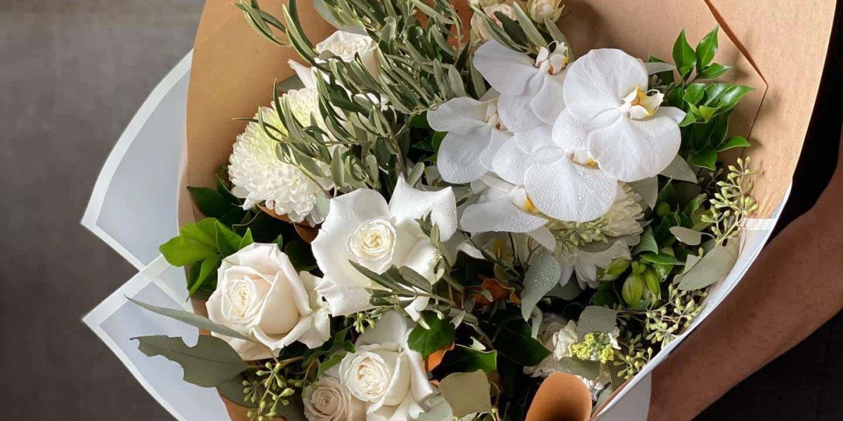A Person is Holding a Bouquet of White Flowers Wrapped in Brown Paper — Suncoast Flowers in Birtinya, QLD