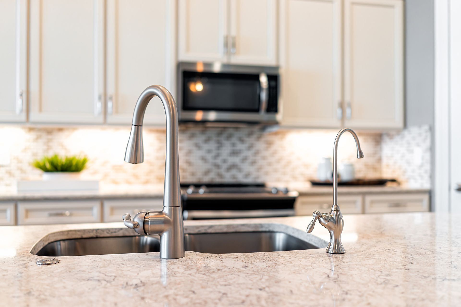 Kitchen sink with two faucets on a light-colored countertop. Stainless steel appliances and white cabinets are in the background.