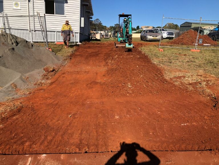 A Man is Standing on a Dirt Road in Front of a House — Burgess Concreting In Blackbutt, QLD