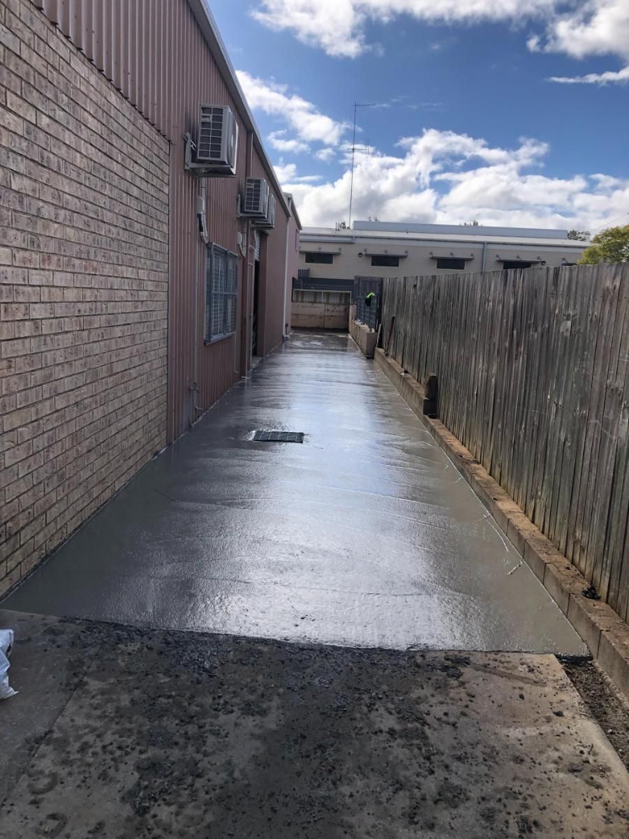 A Concrete Walkway Between Two Buildings With A Fence In The Background — Burgess Concreting In Kingaroy, QLD
